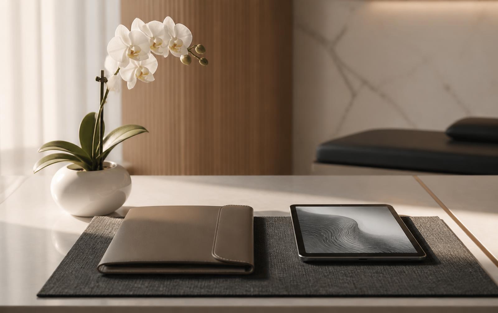 A warm minimal clinic desk with an orchid, leather portfolio and tablet in morning light